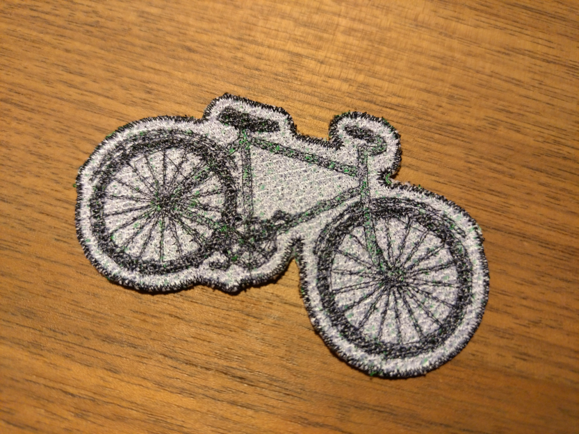 Embroidered patch of a green bicycle as a colorful comic illustration, 8x5 cm
